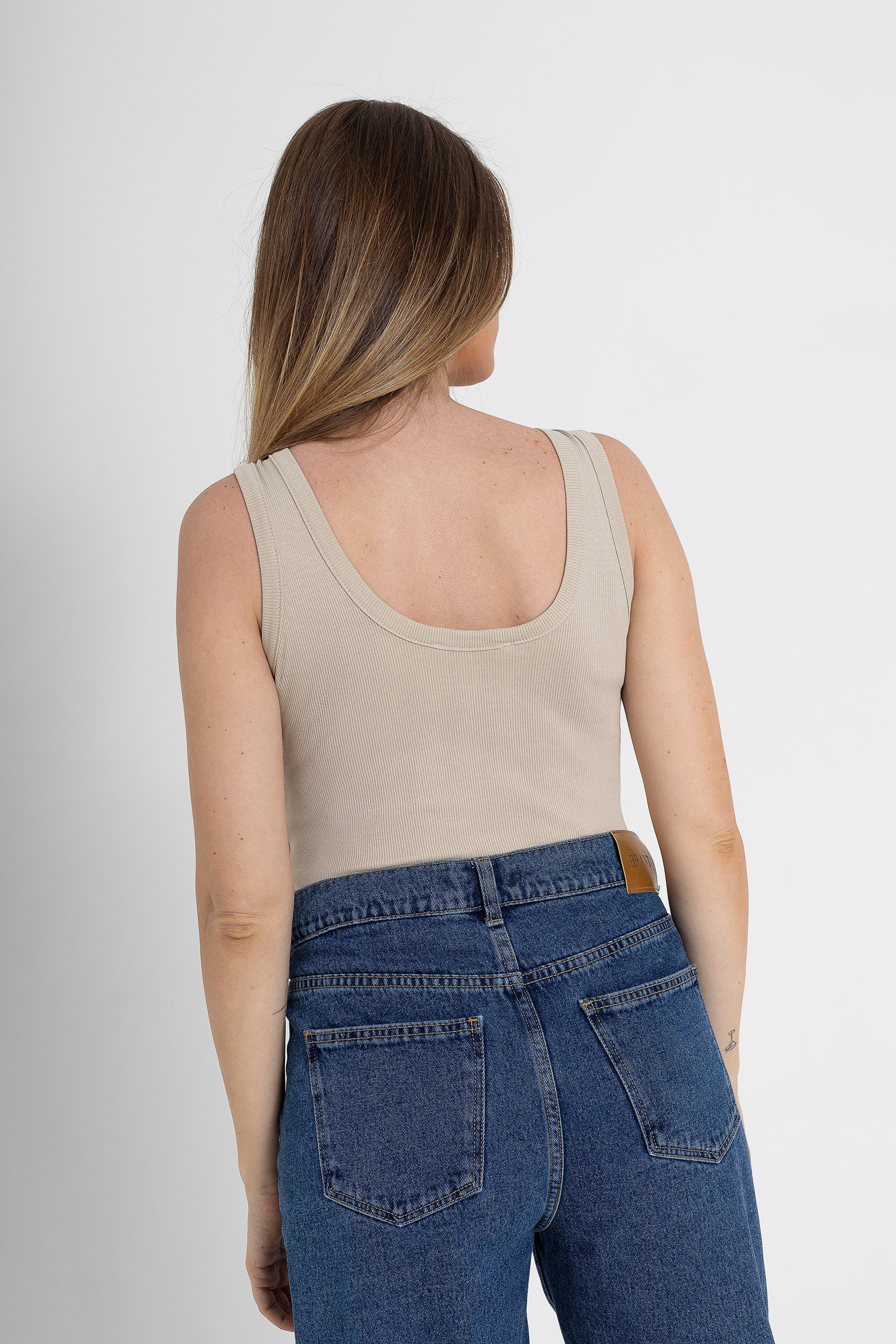Woman wearing a beige tank top and blue jeans from brant against a white background