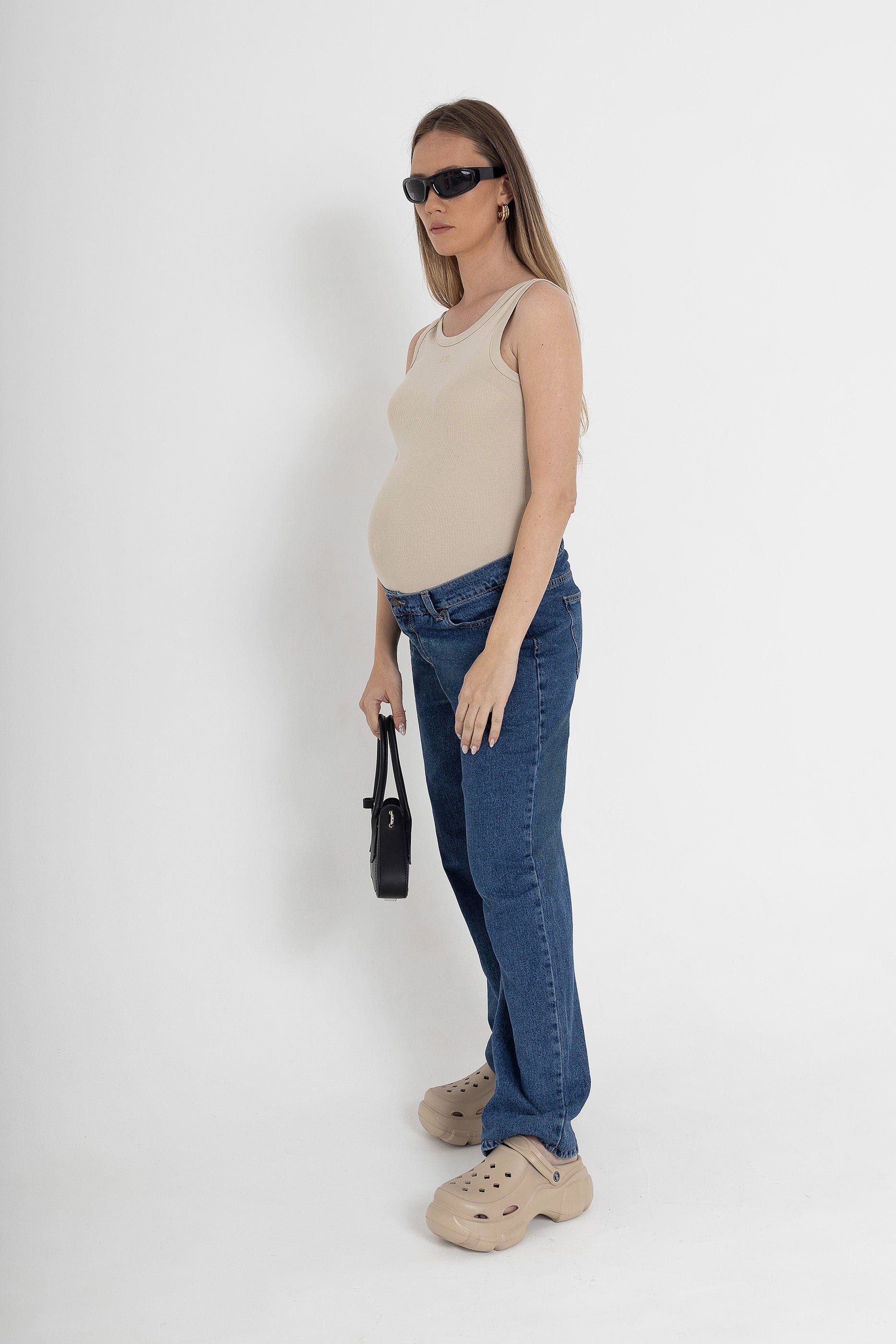 Woman wearing a beige tank top and blue jeans from brant against a white background